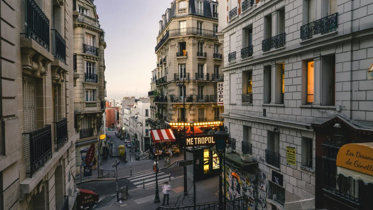 A narrow Paris street at dusk with lit shopfronts along both sides